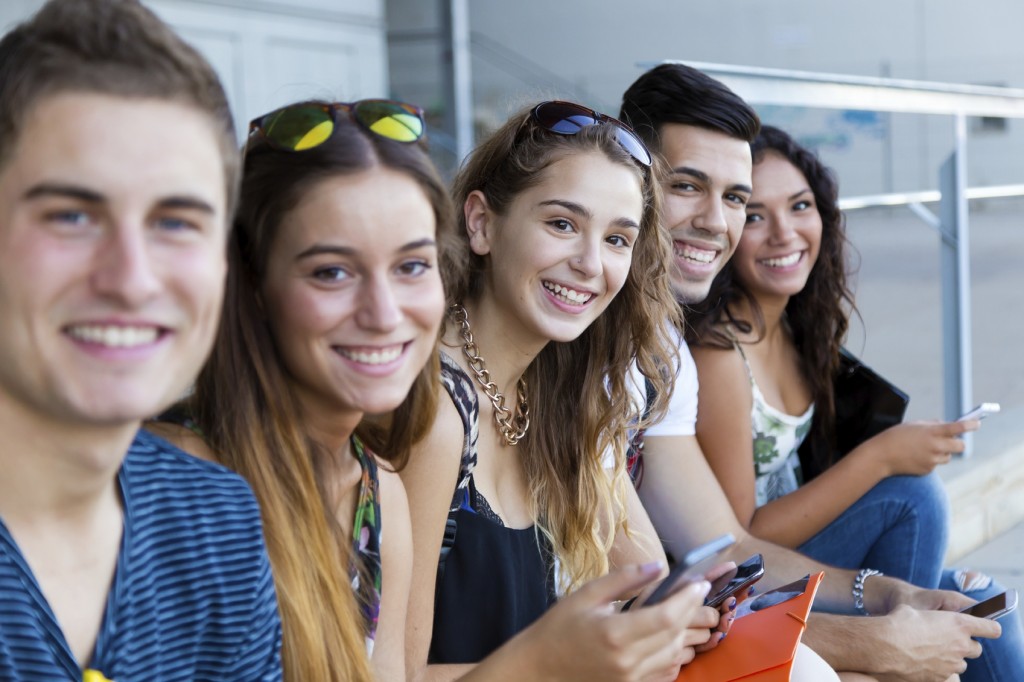 Portrait of group of students having fun with smartphones after class.