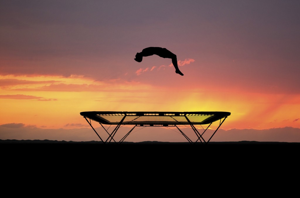 Silhouetted teenager jumping on trampoline in sunset