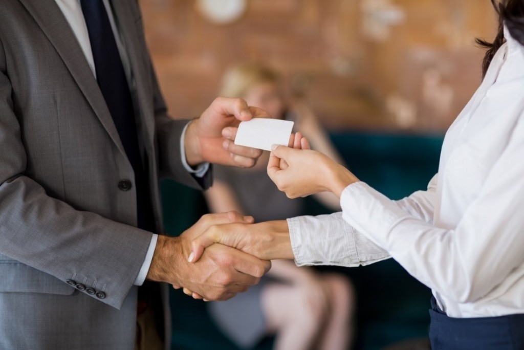 two business professionals shaking hands and handing over a business card